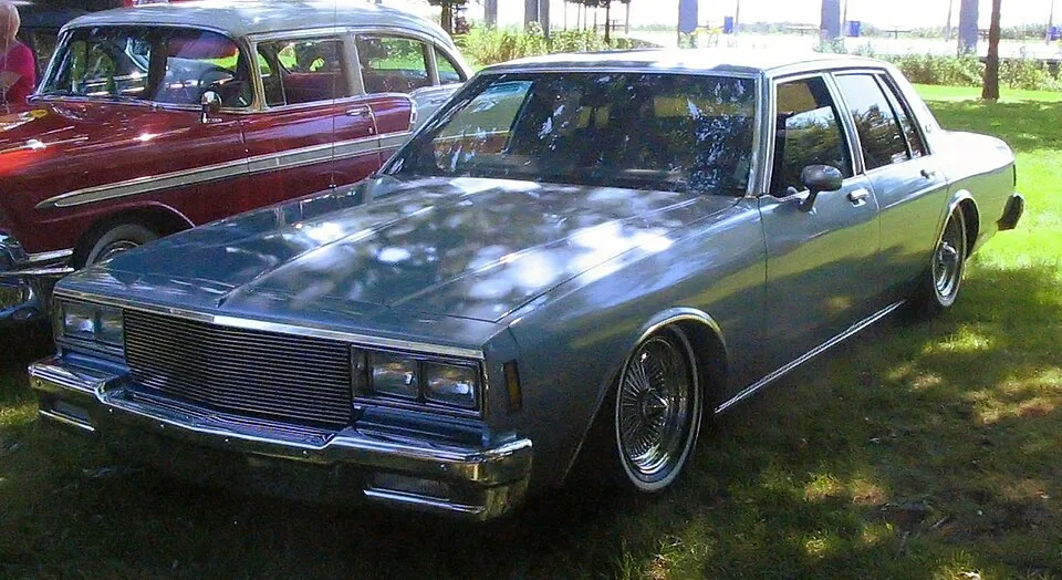 Blue Chevrolet Caprice sedan lowered over wire wheels at a Montreal lowrider gathering.