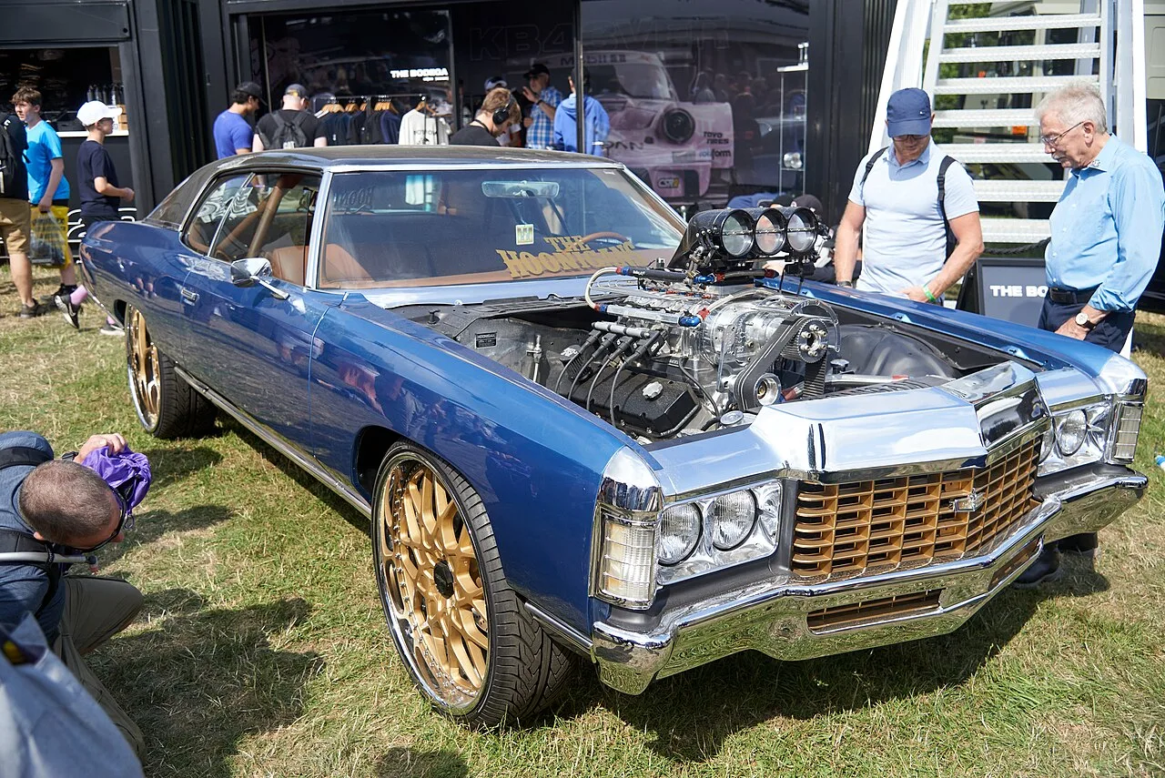 Blue Chevrolet Caprice donk with gold wheels and an exposed engine.